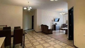 A spacious living area with a tiled floor, a dining table with chairs, and a television in the background. - Nearby Chavchavadze ave Sunny Home With Balcony (Tbilisi)