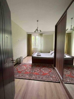 A bedroom with a large mirror, a bed, a chandelier, and a wooden floor.
