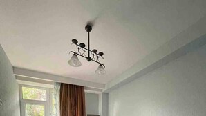 A bedroom with a bed, a nightstand, a lamp, a patterned rug, and a view through a window with curtains. - Nearby Chavchavadze ave Sunny Home With Balcony (Tbilisi)