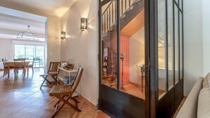 A spacious dining area with a wooden table and chairs, a small white shelf with books, and a view of a staircase leading to a red-lit room. - Cozy home in Villegly with heated swimming pool (Villegly)