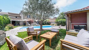 A backyard with a swimming pool, wooden furniture, and a TV. - Cozy home in Villegly with heated swimming pool (Villegly)