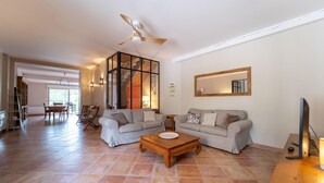 A spacious living room with a high ceiling, a ceiling fan, a large window, a dining area, and a staircase leading to an upper level. - Cozy home in Villegly with heated swimming pool (Villegly)