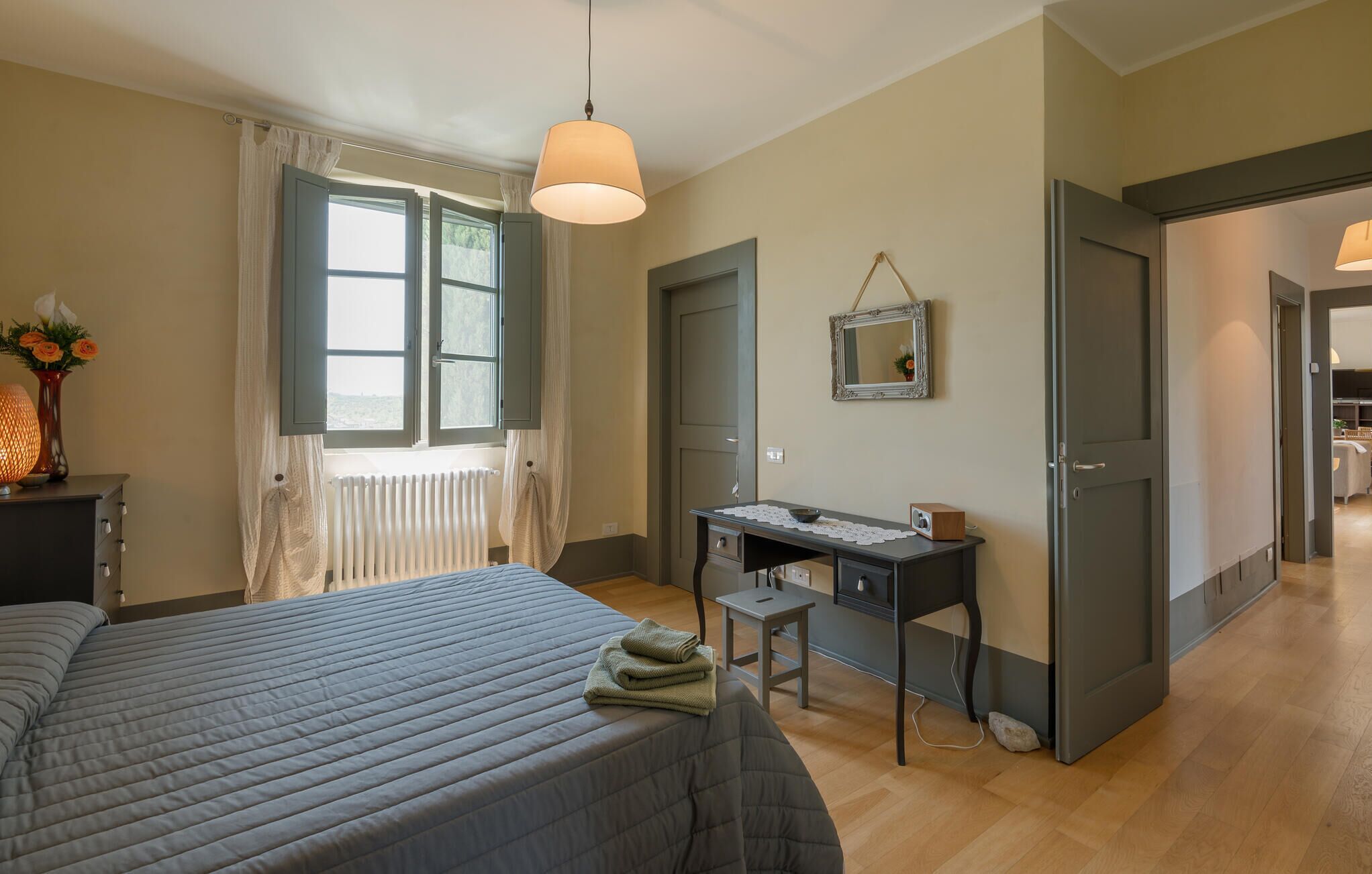 A bedroom with a bed, a desk, a radiator, a mirror, and a window with curtains.