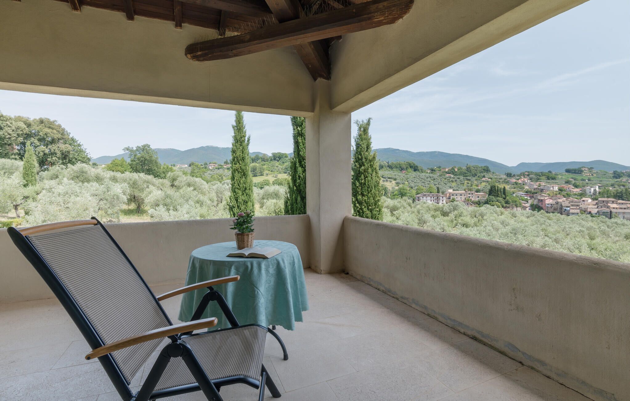 A balcony with a chair and a table, overlooking a scenic landscape with trees and buildings.