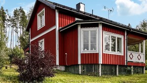 Een rood houten huis met witte raamkozijnen, een schoorsteen en een balkon met een hekwerk.