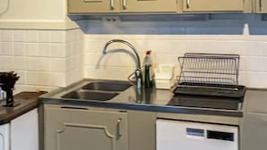 Een keuken met een roestvrijstalen spoelbak, een afdruiprek en een vaatwasser.