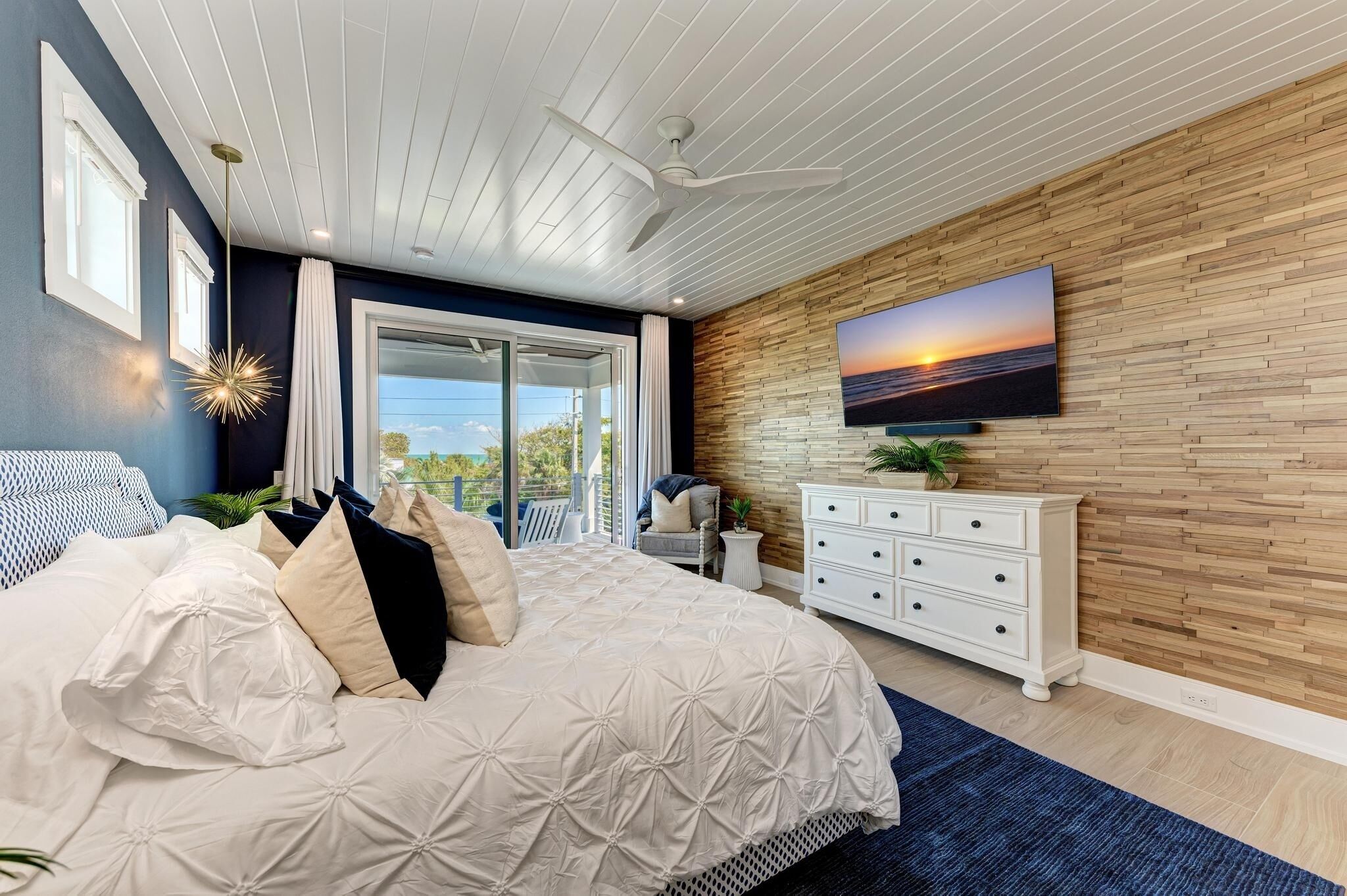 Ein Schlafzimmer mit einem großen Bett, einer Holzwand, einem Fernseher und Blick ins Freie.