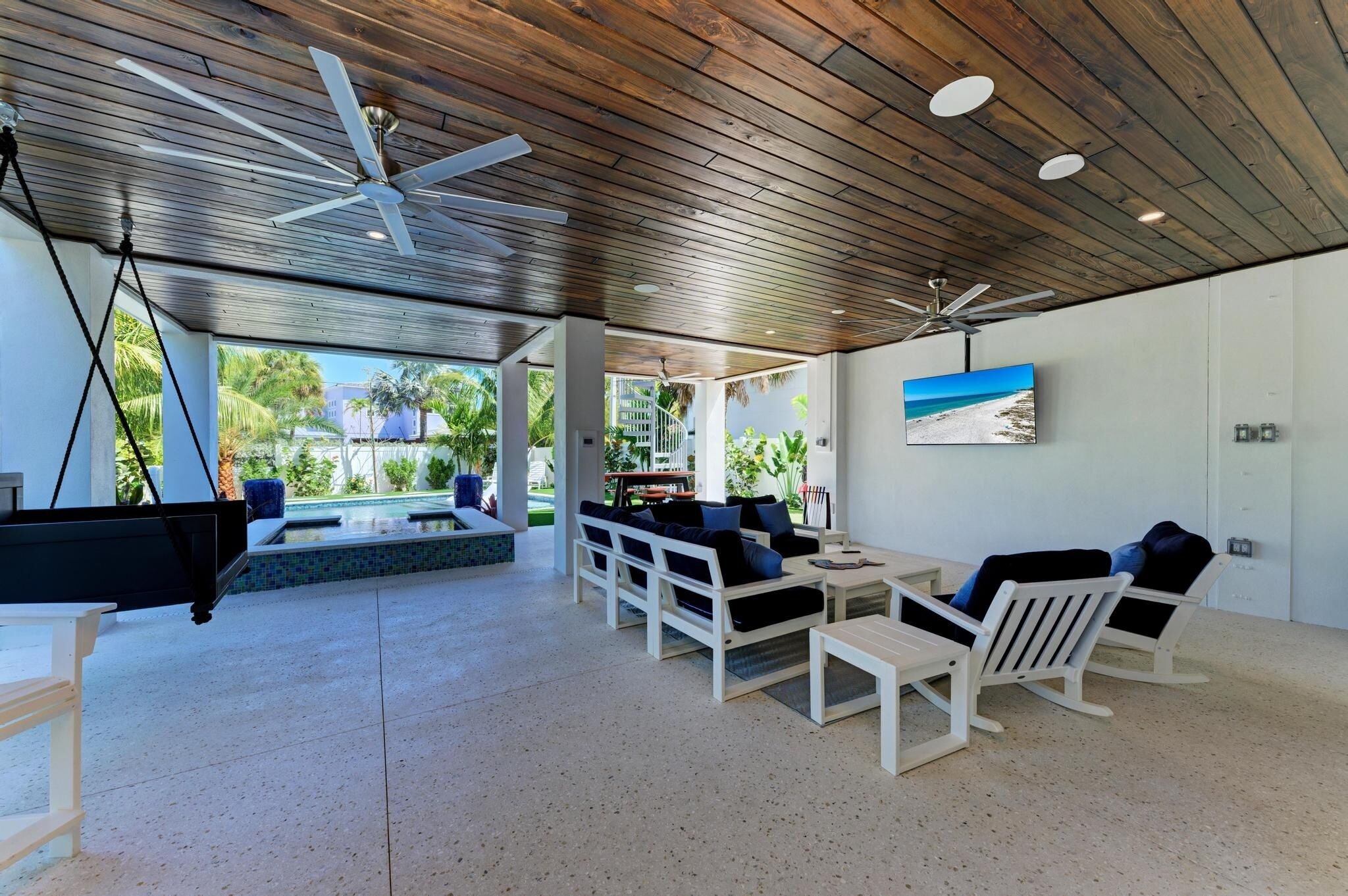 A spacious indoor area with a pool, outdoor seating, ceiling fans, and a mounted TV.