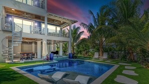 Una casa moderna de dos pisos con piscina, mobiliario exterior y un césped cuidado.