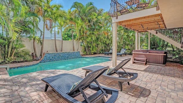 A pool area with lounge chairs, a hot tub, and a staircase leading to a balcony. - Angel Sea managed by Beach Retreats (Holmes Beach)