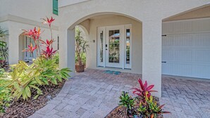 A covered patio area with a tiled floor, a white garage door, and various potted plants. - Angel Sea managed by Beach Retreats (Holmes Beach)