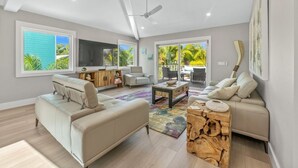 Ein geräumiges Wohnzimmer mit Sofa, Couchtisch und Fernseher. Große Fenster und ein Balkon mit Blick auf Grünflächen.
