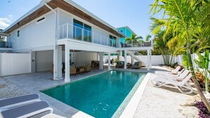 Ein modernes, zweistöckiges Haus mit Swimmingpool, Sitzgelegenheiten im Freien und tropischer Bepflanzung.