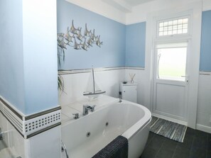A modern bathroom with a freestanding bathtub, a decorative wall piece, and a window with a view. - Russell House (Paignton)