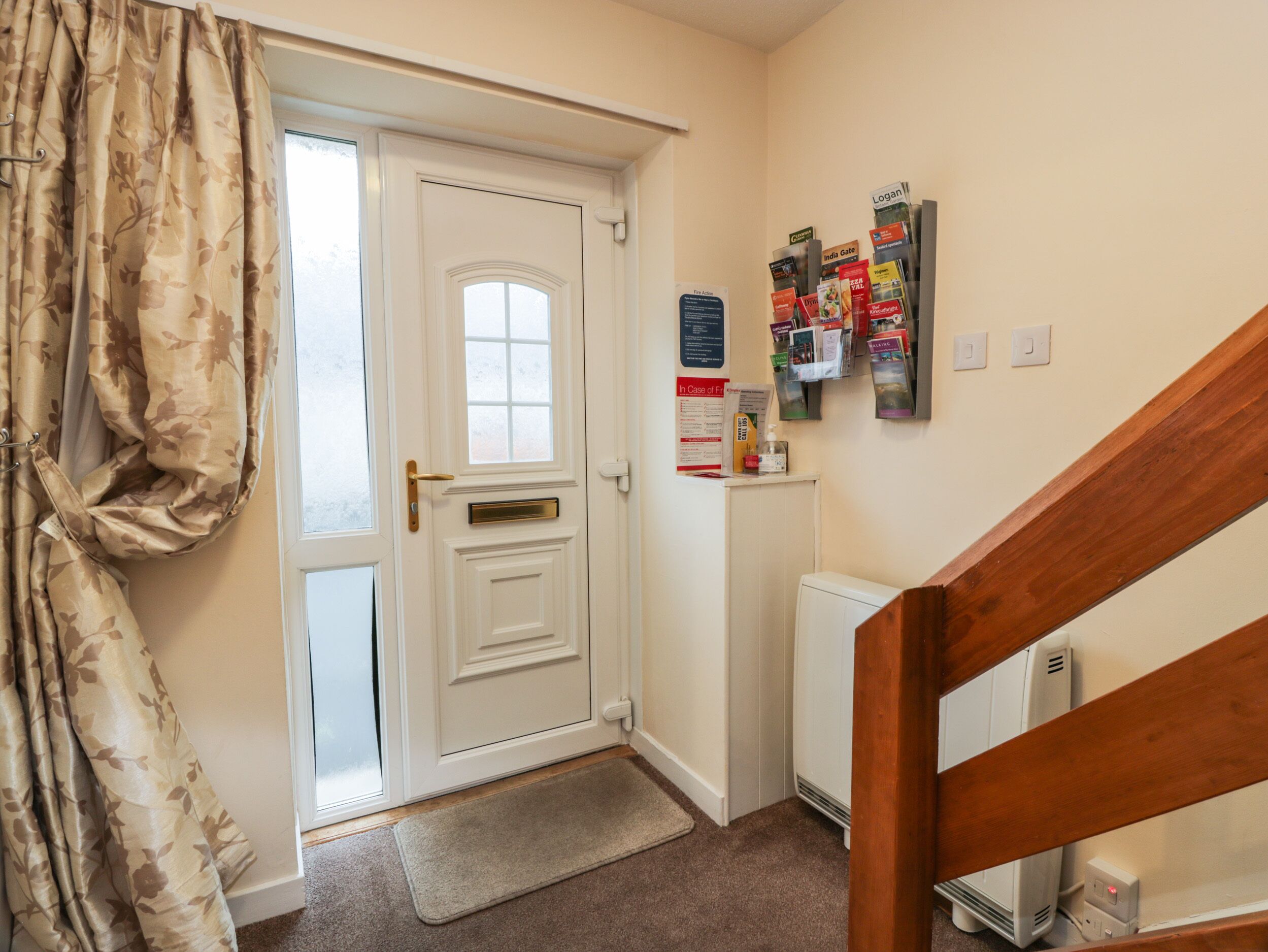 A hallway with a white door, a bulletin board with various pamphlets, a radiator, and a wooden staircase.