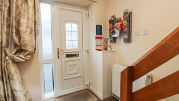 A hallway with a white door, a bulletin board with various pamphlets, a radiator, and a wooden staircase.