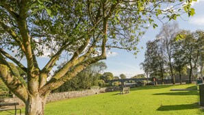 A grassy park area with a large tree, a stone wall, and a bench. - Barley Cottage (Newton Stewart)