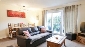 A living room with a dark leather sofa, a wooden coffee table, and a dining area with a table and chairs. - Barley Cottage (Newton Stewart)