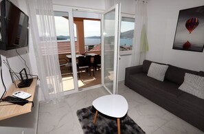 Un soggiorno moderno con un divano, un tavolino bianco, una televisione e un balcone vista mare.