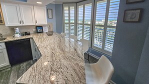 A kitchen with a curved marble countertop, white cabinets, and a view through large windows. - 108 Brighton 3 Bedroom Condo (Myrtle Beach)