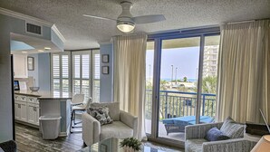 A spacious living area with a balcony, a kitchen in the background, and a ceiling fan. - 108 Brighton 3 Bedroom Condo (Myrtle Beach)