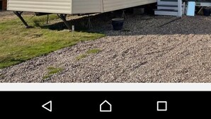 A mobile home with a satellite dish, a small porch, and a gravel driveway. - Daisy's Luxury Caravan (Lincoln)