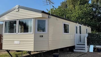 A mobile home with a front porch, a satellite dish, and a small deck.