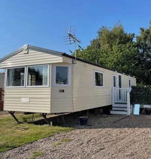 A mobile home with a front porch, a satellite dish, and a small deck. - Daisy's Luxury Caravan (Lincoln)