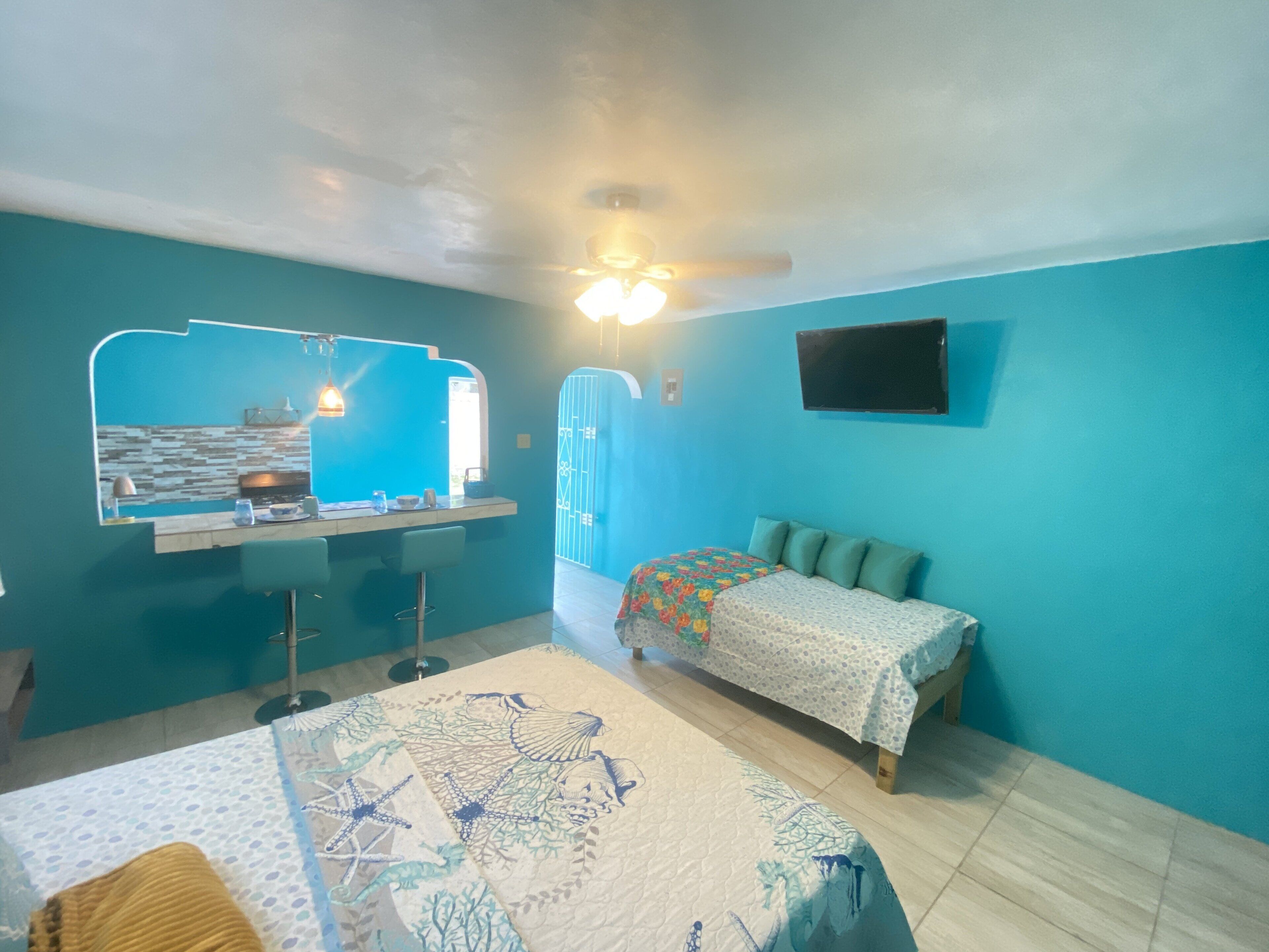 Quarto com cama, mesa de cabeceira, cadeira, escrivaninha, espelho, janela e ventilador de teto.