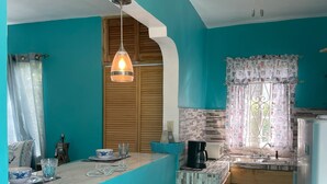 A kitchen with teal walls, a wooden ceiling fan, and a window with patterned curtains. - YanceyLargo Estate - Newly Built Modern 1 Bedroom Suite 1 Villa by RedAwning (Montego Bay)