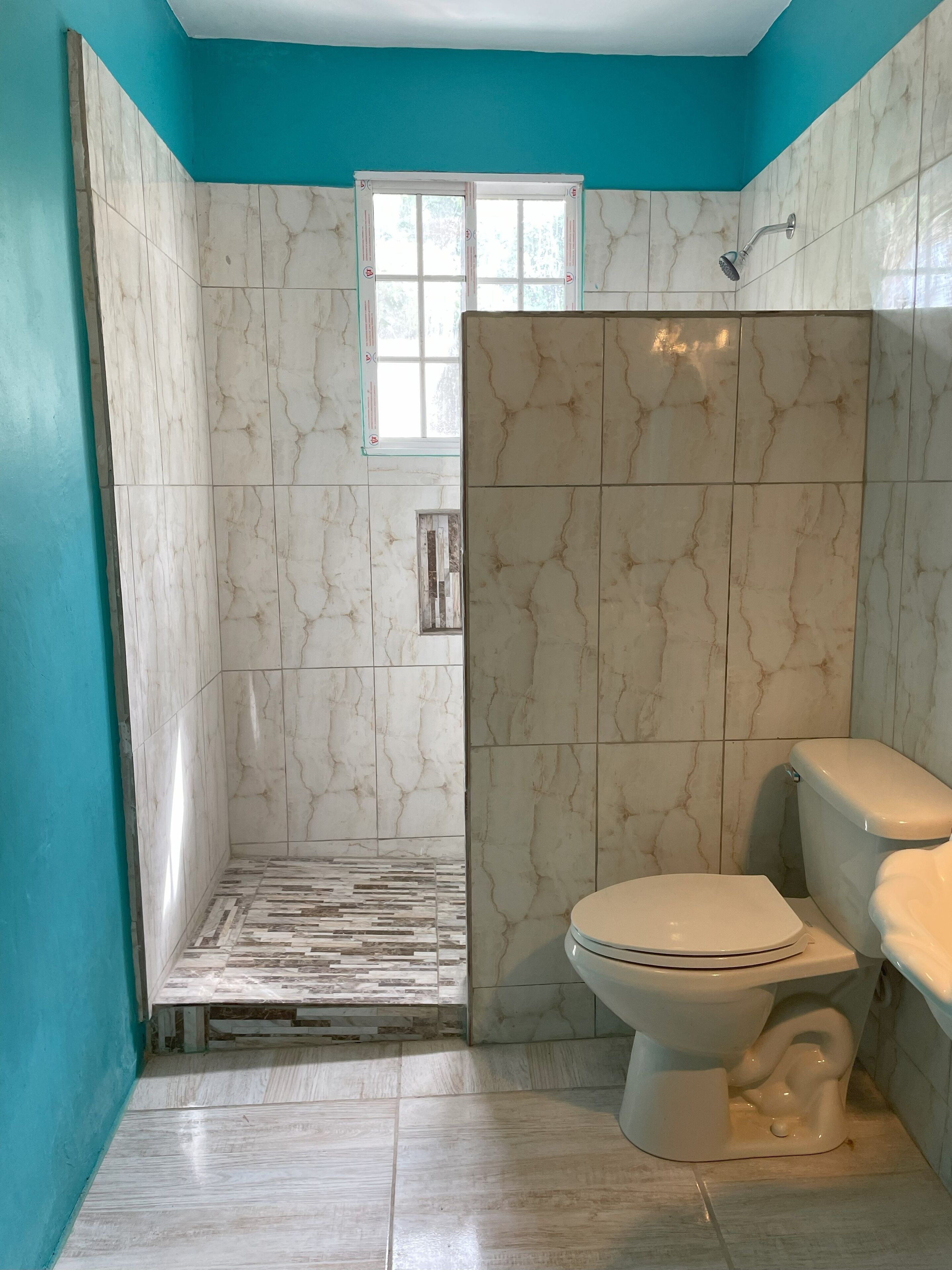 Un baño con paredes de mármol blanco, zona de ducha y un inodoro.
