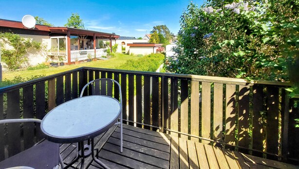 A wooden deck with a table and chairs, surrounded by a wooden fence and lush greenery.