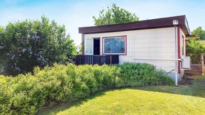 A small, single-story building with a sloped roof, a wooden deck, and a window with a view of the surrounding greenery.
