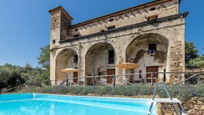 A stone building with arched windows and a pool in front.