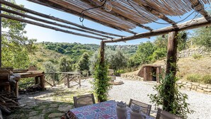 An outdoor patio with rustic wooden furniture, a table with a colorful tablecloth, and a pergola overhead.