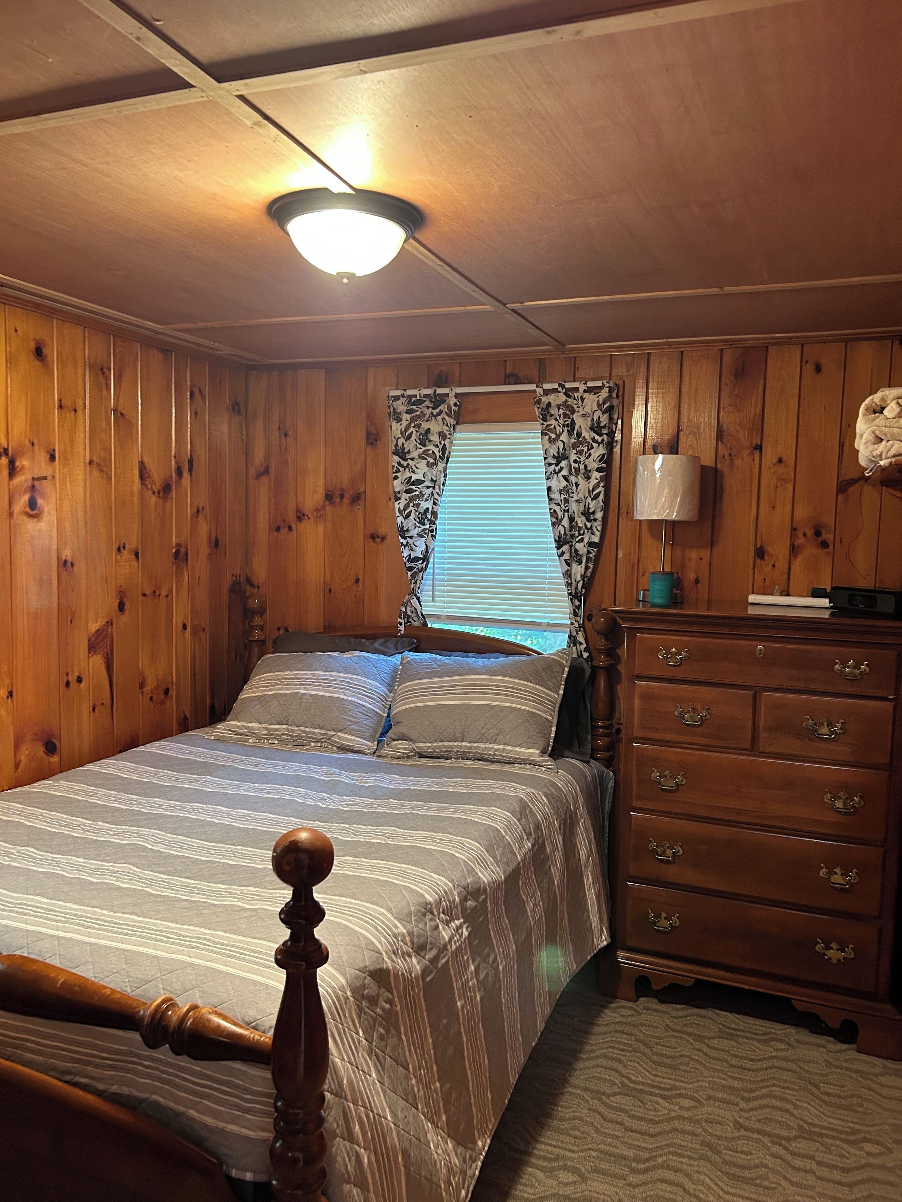 A wooden-paneled bedroom with a bed, a dresser, and a window with curtains.
