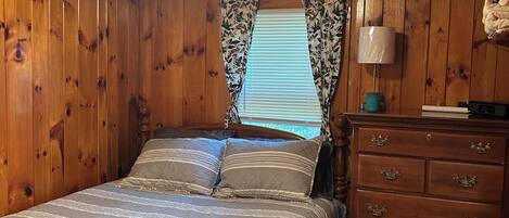 A wooden-paneled bedroom with a bed, a dresser, and a window with curtains.