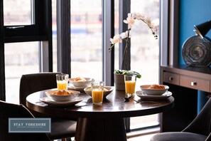 A breakfast table with plates, glasses, and a vase of flowers, set in a room with a window and a plant. - Blonk Street Apartments  (Sheffield)