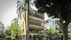 Un immeuble résidentiel à plusieurs étages, doté de balcons, d’un passage piéton et de véhicules stationnés.