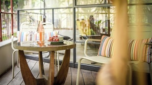 Une table ronde avec une bouteille, des verres et une assiette de raisins, placée sur un balcon d’où l’on peut admirer la verdure.