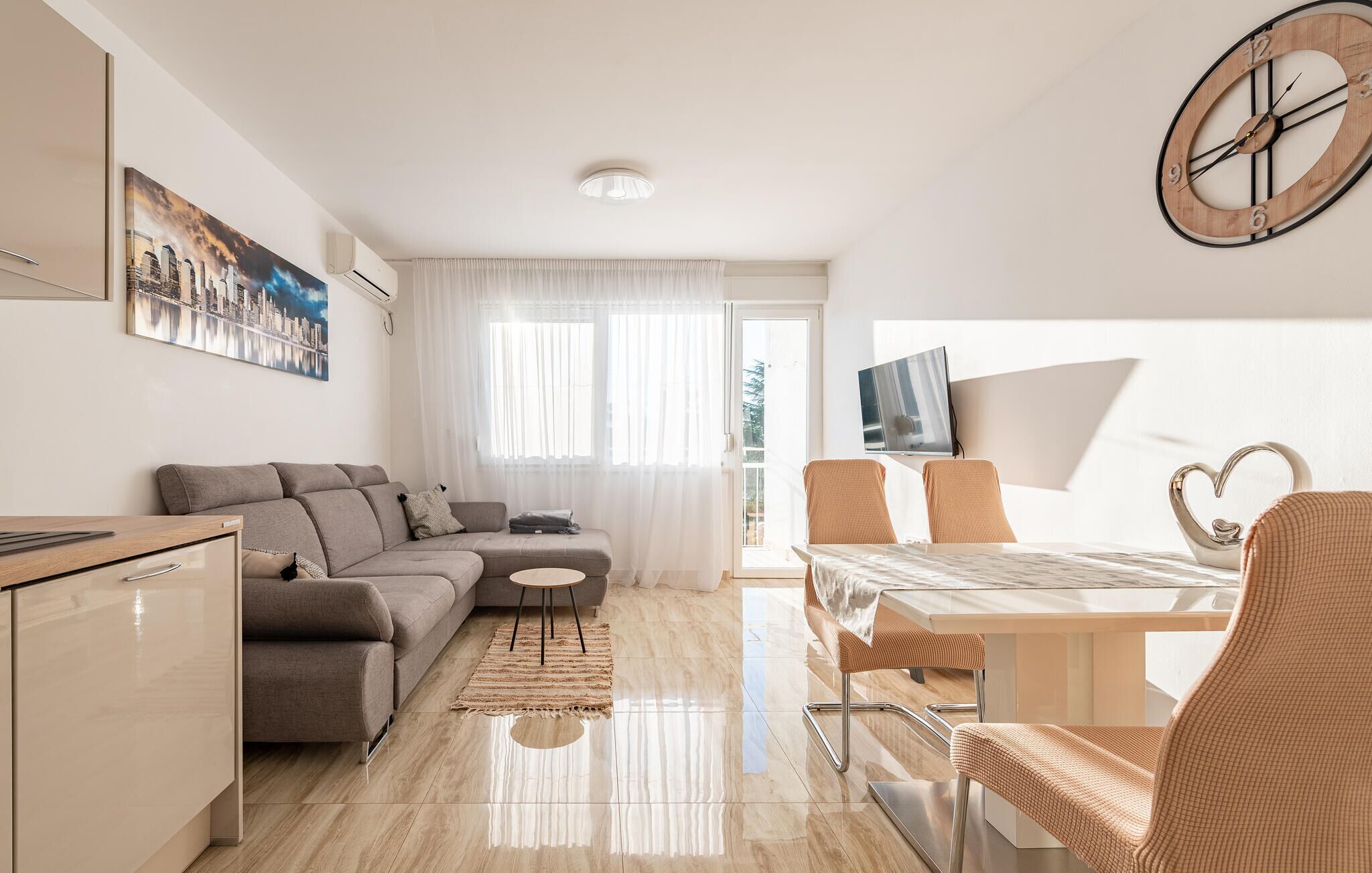 A modern living room with a sofa, a dining table with chairs, a TV, and a clock on the wall.