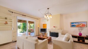 A living room with two sofas, a television, a fireplace, and a painting on the wall. - Stunning 5-bed Villa in Gennadi! (Rhodes)