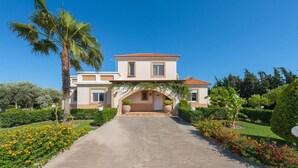 A two-story house with a central archway, surrounded by well-maintained gardens and a clear sky. - Stunning 5-bed Villa in Gennadi! (Rhodes)