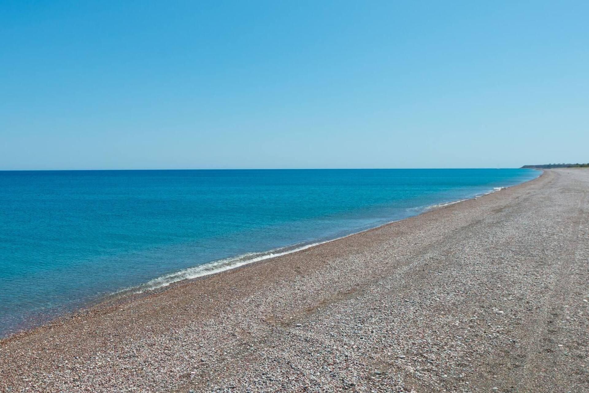 A pebbled beach with clear blue water and a clear sky.