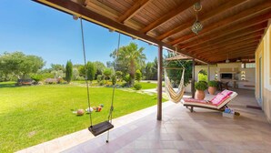 A covered patio with a swing, a lounge chair, and a view of a well-maintained lawn and garden. - Stunning 5-bed Villa in Gennadi! (Rhodes)