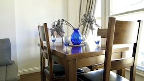 A dining table with a blue vase and two glasses, surrounded by wooden chairs.