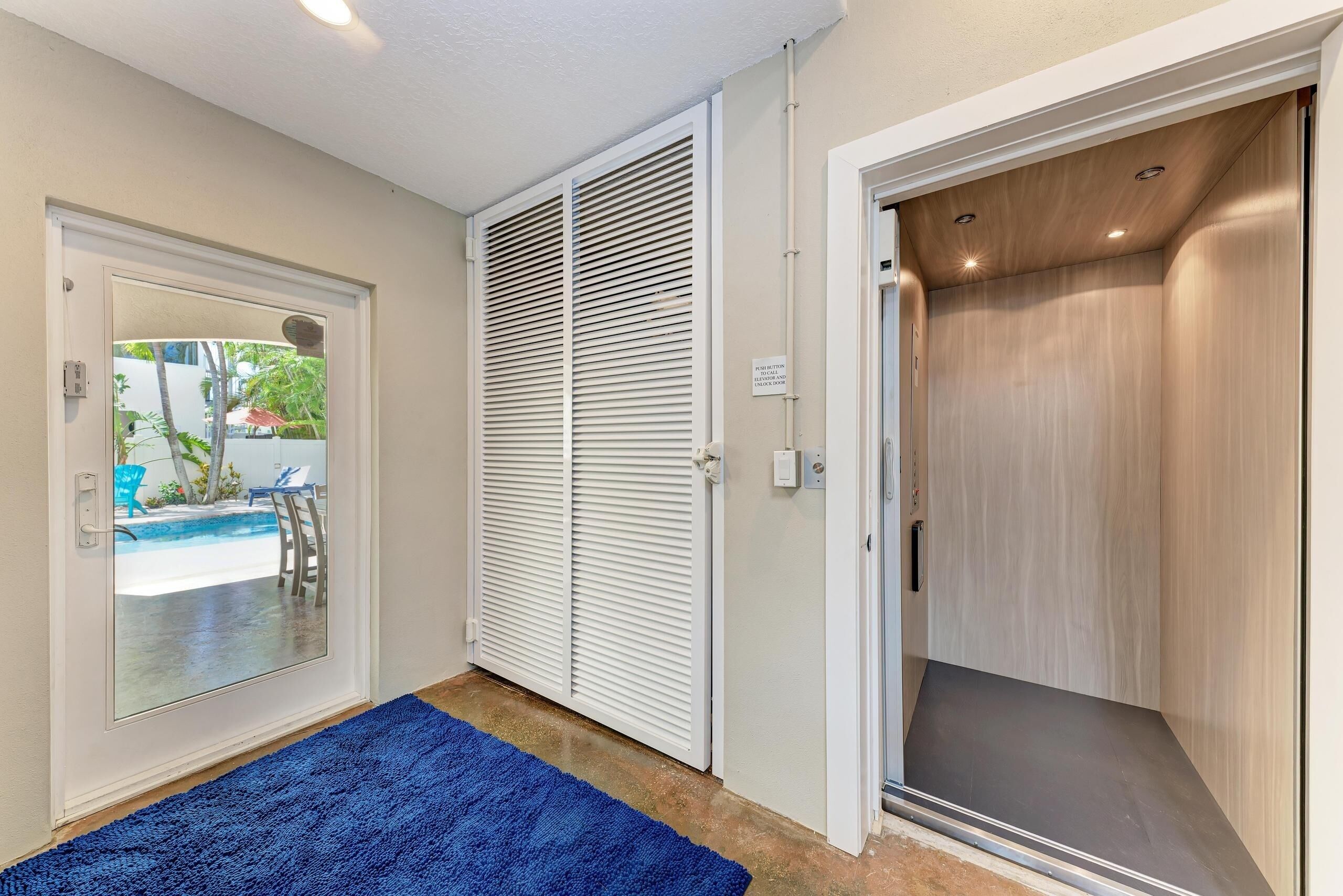 A room with a sliding door leading to a pool area, a blue rug, and a wooden elevator.