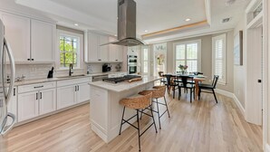 Une cuisine spacieuse avec des meubles blancs, un îlot central doté de tabourets, et un coin repas avec une table et des chaises.