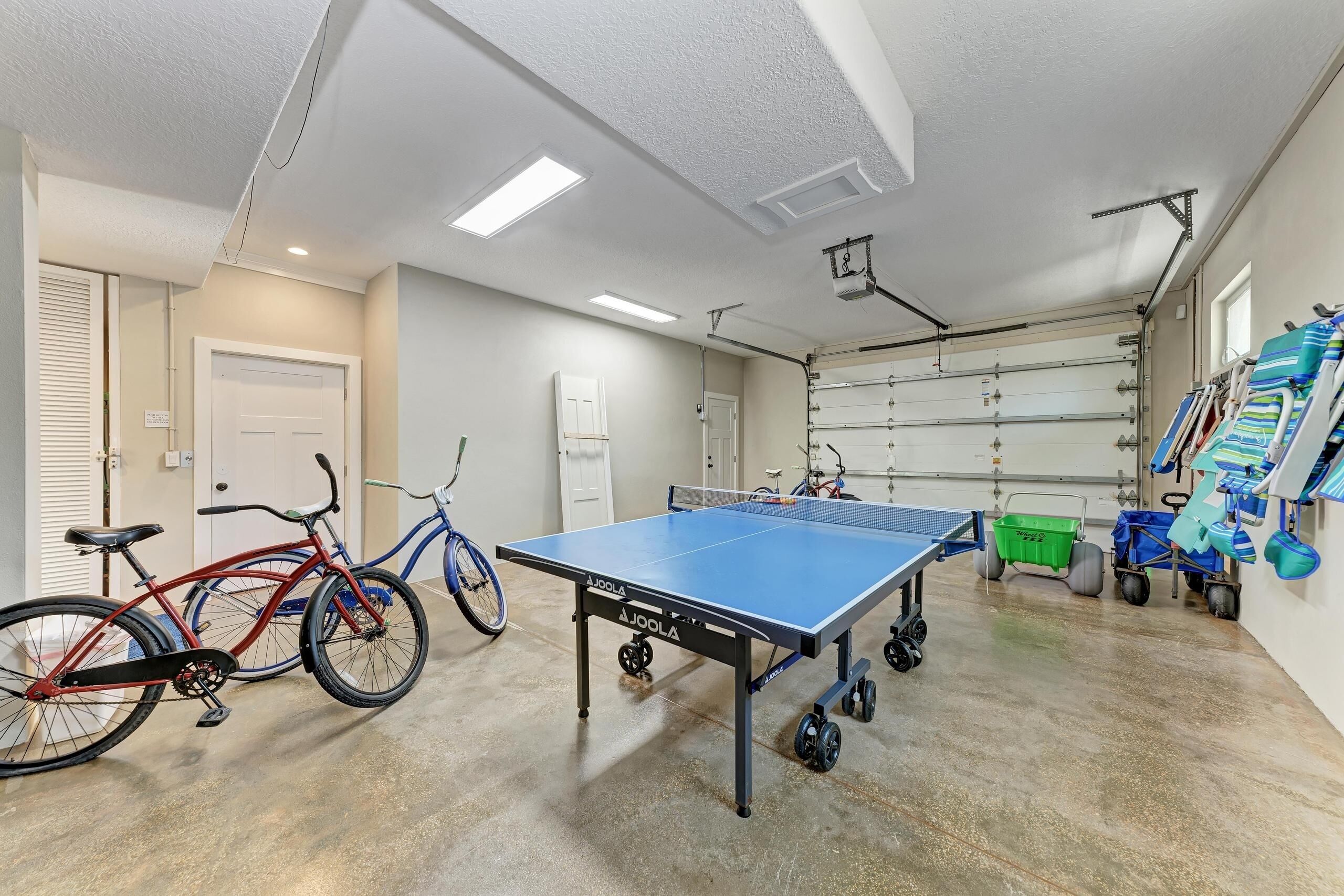 A spacious indoor area with a ping pong table, bicycles, and a garage door.