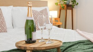 A bed with a wooden bedside table holding a bottle and two glasses. - Ty Arth (Llandudno)